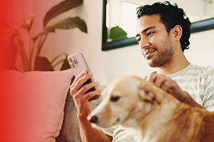 Hombre usando su celular en el sillón junto a su perro después de pasarse a Claro con su mismo número